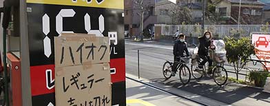 A sold-out note is pasted on a gas price board as bicyclers pass by a gas station in Tokyo, Wednesday, March 16, 2011.