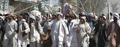 Protestors walk with sticks, as they carry a wounded colleague during a demonstration to condemn the burning of a copy of the Muslim holy book by a Florida pastor, in Kandahar, Afghanistan on Saturday, April 2, 2011. (AP Photo/Allauddin Khan)