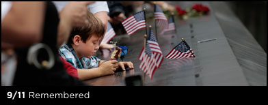 A young boy is surrounded by flags, rock and people as he leans on one of the perimeter walls surrounding a reflecting pool at the Sept. 11 memorial in New York, Sunday, Sept. 11, 2011. Sunday marked the 10th anniversary of the terrorists attacks on the World Trade Center. (AP Photo/Chip Somodevilla, Pool)