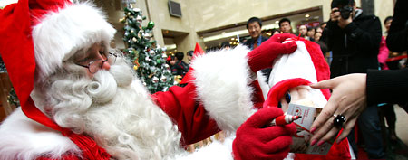 Nicholas from Finland, who was dressed as the Santa Claus, presents a gift to a customer during a promotion in a department store. (Photo by China Photos/Getty Images)