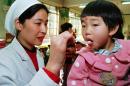 FILE - In this Wednesday, Dec. 6, 1995 file photo, Dr. Lai Nansha uses a spoon to administer a polio vaccination pill to a child at a kindergarten in Beijing. (AP Photo/Greg Baker)