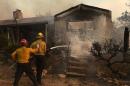 A firefighter sprays a smoldering home as the Erskine Fire burns near Weldon
