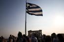 Greek flag flutters in the wind above tourists visiting the archaeological site of the Acropolis hill in Athens, Greece