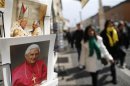Tourists walk past pictures of Pope Benedict XVI displayed in a shop in Rome