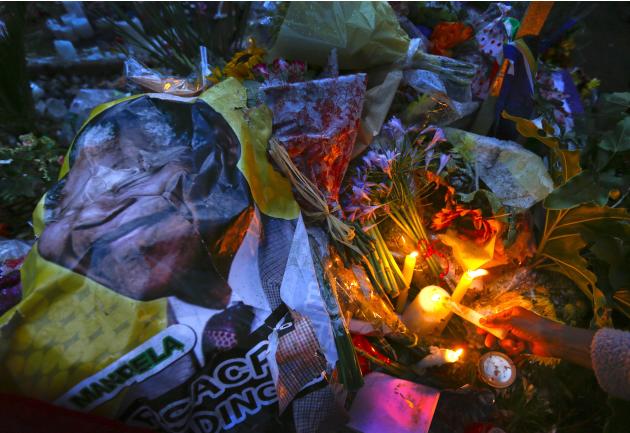 A mourner places a candle on a pile of flowers and photos of Mandela during a homage outside the Houghton home of the late former South African President Nelson Mandela in Johannesburg
