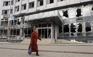 A woman walks past a building damaged by fighting in &hellip;