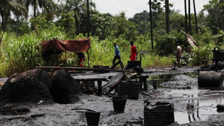 In this photo taken Saturday, May 18, 2013, men walk past an abandoned illegal refinery at the creeks of Bayelsa, Nigeria. The first drops of crude float in the languid muddy currents of Nigeria's oil-rich southern delta, then slowly grow into the splatter of massive crime scene. Oil thefts, long a problem in the Niger Delta, are growing at an ever-faster rate despite government officials and international companies offering increasingly dire warnings about the effect on Nigeria's crude production. Some 200,000 barrels a day representing about 10 percent of Nigeria's production are siphoned off pipelines crisscrossing the region. (AP Photo/Sunday Alamba)