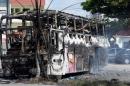 A police vehicle stands behind a smouldering bus after it was set on fire during violent overnight disturbances in Natal
