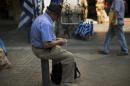 A man counts money as he sits in front of a shop selling Greek flags in central Athens, Tuesday, July 14, 2015. Prime Minister Alexis Tsipras was seeking Tuesday to rally his party members to support a preliminary rescue deal struck with Greece's European creditors that includes measures so onerous some of his own ministers were in open revolt. (AP Photo/Emilio Morenatti)