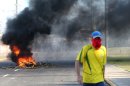 A masked protestor walks near a burning barricade as riot police stand guard near the Castelao stadium in Fortaleza, Brazil, Wednesday, June 19, 2013. Protesters cut off the main access road to the stadium where Brazil goes up against Mexico in the Confederations Cup soccer tournament. Beginning as protests against bus fare hikes, the demonstrations have quickly ballooned to include broad middle-class outrage over the failure of governments to provide basic services and ensure public safety. (AP Photo/Andre Penner)