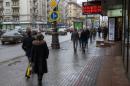 People walk under under a board listing foreign currency rates against the Russian ruble just outside an exchange office in central Moscow on February 14, 2014