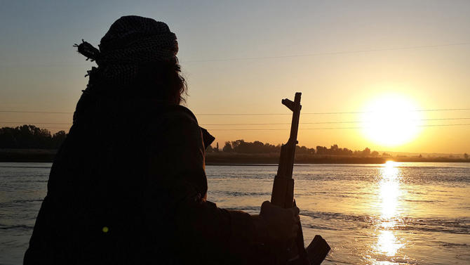 In this photo released on Sept. 29, 2014 by a militant website, which has been verified and is consistent with other AP reporting, an Islamic State group fighter holds his AK-47 machine gun as he relaxes on the bank of the Euphrates river in Raqqa, Syria. The IS group has set up a generous welfare system to help settle and create lives for the thousands of jihadis, men and women, who have flocked to IS territory from the Arab world, Europe, Central Asia and the United States. (Militant website via AP)