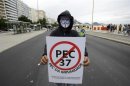 A protester wearing a Guy Fawkes mask holds a sign protesting proposed constitutional amendment PEC 37 at the Copacabana beach in Rio de Janeiro