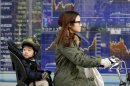 A mother and child cycle past an electronic stock board of a securities firm in Tokyo, Monday, Jan. 21, 2013. Asian stock markets were mixed Monday amid uncertainty about the outcome of a central bank meeting in Japan and nervousness over whether U.S. political leaders will be able to reach a deal on the government's debt limit. (AP Photo/Koji Sasahara)