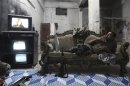 A Free Syrian Army fighter rests on a sofa as he watches televison and surveillance monitors inside a room in Aleppo's Karm al-Jabal district