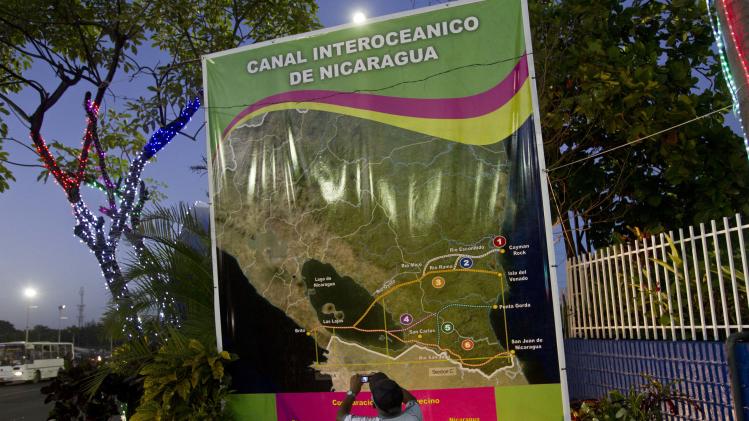 In this Dec. 4, 2013 photo, Oscar Torres, a 62-year-old retired construction worker takes photos of a banner showing a map of Nicaragua with possible routes of the Inter-Oceanic canal in Managua, Nicaragua. Six months after the Sandinista government granted a Chinese businessman a 100-year concession to build a vast canal across the country, Nicaraguans are confident the $40 billion canal will become reality, lifting their country from poverty to prosperity. (AP Photo/Esteban Felix)