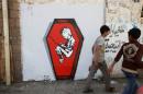 Boys walks pass a graffiti of artist Murad Subai depicting a child suffering from malnutrition in a coffin along a street in Sanaa, Yemen