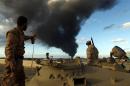 Members of the Libyan army stand on a tank as heavy black smoke rises from the city's port in the background after a fire broke during clashes against Islamist gunmen in the eastern city of Benghazi on December 23, 2014