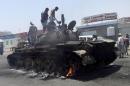 People stand on a tank that was burnt during clashes on a street in Yemen's southern port city of Aden