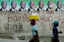 Haitians walk past posters of presidential candidate Guy Philippe at a street in Port-au-Prince