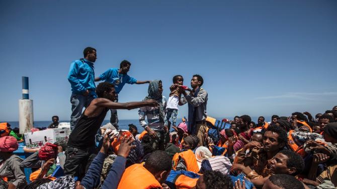 Migrants sit aboard a wooden boat during a rescue operation, in partnership with Doctors Without Borders (Medecins Sans Frontieres, MSF), off the coast of Sicily in the Mediterranean sea, in May 2015