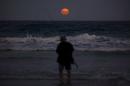 A fisherman prepares to cast his line standing in the surf as a full moon rises at Mollymook Beach, located south of Sydney, Australia