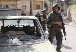 Lebanese Army soldiers walk past a damaged car as they are deployed after clashes in south Beirut