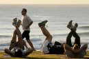 Jogger passes fitness enthusiasts performing stretching exercises after sunrise at Queenscliff Beach in Sydney