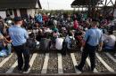 Policemen stand guard as migrants wait at a railway station near the official border crossing between Serbia and Croatia on September 17, 2015