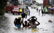 Un grupo de personas trata de no mojar sus pertenencias al cruzar una calle completamente inundada en la ciudad de Quezón (Filipinas). EFE/Archivo