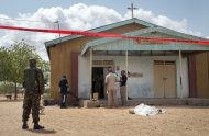 Members of the Kenyan security forces inspect the scene, as a body lies covered by a sheet, outside the African Inland Church in Garissa, Kenya Sunday, July 1, 2012. Gunmen killed two policemen guarding a church, snatched their rifles and then opened fire on the congregation with bullets and grenades on Sunday, killing at least 10 people and wounding at least 40, security officials said, with militants from Somalia being immediately suspected. (AP Photo/Chris Mann)