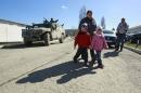 A woman with children walks by a military personnel member, believed to be a Russian serviceman, who stands guard on a military vehicle outside the territory of a Ukrainian military unit in the village of Perevalnoye outside Simferopol