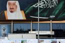 A worker stands beneath an image of Saudi King Salman in Riyadh, Saudi Arabia, Tuesday, April 19, 2016. (AP Photo/Hasan Jamali)