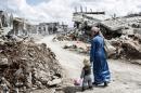 A Kurdish Syrian woman walks with her child past the ruins of the town of Kobane, also known as Ain al-Arab, on March 25, 2015