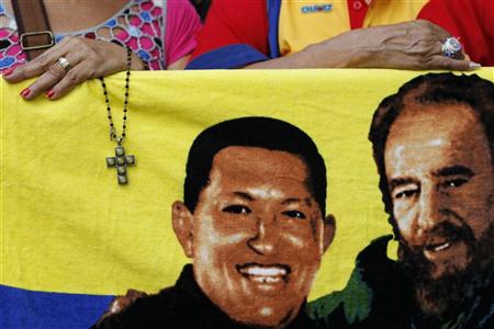 Apoiador do presidente venezuelano, Hugo Chávez, segura crucifixo perto da imagem de Chávez e do ex-líder Fidel Castro (D), em Caracas. Chávez segue acamado em Cuba enquanto seus partidários se preparam para uma grande demonstração de apoio no dia em que ele deveria tomar posse para um novo mandato de seis anos. 05/01/2013 REUTERS/Carlos Garcia Rawlins