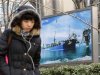 A woman walks past a poster showing an offshore work platform from CNOOC in Beijing