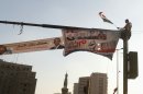 A man sits on a lamppost as he waves an Egyptian flag near banners in Tahrir square, in Cairo