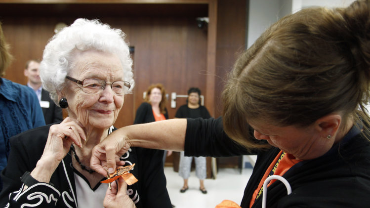 In this Sept. 23, 2013, Audrey Crabtree, 99, left, smiles as Sarah Dierks pins a 1972 East High homecoming pin onto her jacket during an during an education board meeting in Waterloo, Iowa, where she received an honorary diploma. Crabtree dropped out of a Waterloo high school in 1932 due to an injury and to care for her grandmother. She went on to run her own business for nearly three decades. (AP Photo/Waterloo Courier, Tiffany Rushing)