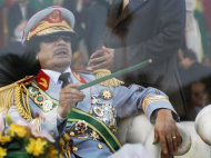 FILE - In this Tuesday, Sept. 1, 2009 file photo, Libyan leader Moammar Gadhafi gestures with a green cane as he takes his seat behind bulletproof glass for a military parade in Green Square, Tripoli, Libya. Libyan special forces stormed a two-day-old protest encampment in the country's second largest city of Benghazi, clearing the area early Saturday, Feb. 19, 2011, said witnesses, as a human rights group estimate scores of people have died in the harsh crackdown on days of demonstrations.