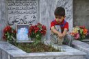 A boy sits on a grave of his brother, who was killed by gunmen, at the Hazara graveyard in Mehrabad