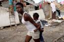 A woman carries a child as they walk in front of destroyed houses after Hurricane Matthew passes Jeremie