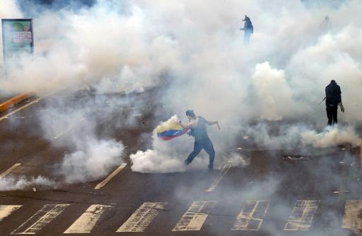 Un manifestante con una bandera venezolana devuelve un contenedor de gas lacrimógeno hacia la Guardia Nacional Bolivariana mientras ésta dispersaba una protesta en una autopista importante de Caracas, Venezuela, el jueves 27 de febrero de 2014. (Foto AP/Fernando Llano)