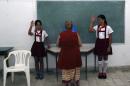 School children salute as a woman casts her ballot during Cuba's municipal elections at a polling station in Havana, Cuba, Sunday, April 19, 2015. Cuba held its first local elections since a historic thaw in relations with the United States with an unusual wrinkle in the single-party system: two of the 27,000 candidates openly oppose the government. (AP Photo/Desmond Boylan)