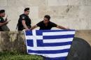 An anti-EU protester unfurls a Greek national flag next to riot police on the steps in front of the parliament building during a demonstration of about five hundred people in Athens