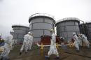 File photo of members of the media and TEPCO employees wearing protective suits and masks walking past storage tanks in Fukushima prefecture
