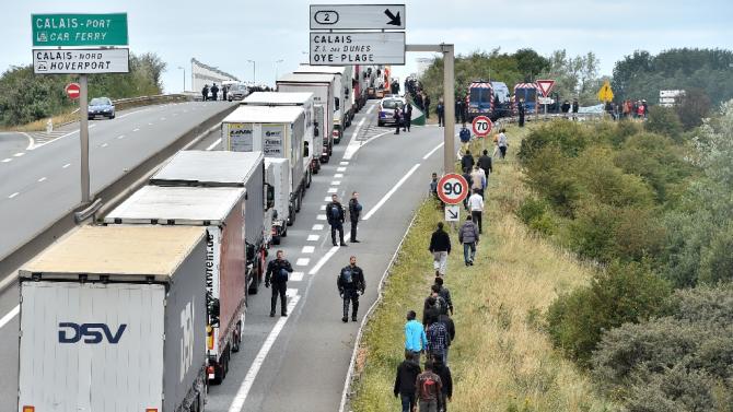Police officers stand on the road to prevent migrants from climbing aboard trucks travelling to Britain on ferries or the nearby Channel Tunnel shuttle train in Calais on August 20, 2015