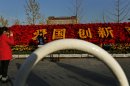 In this photo taken Monday, Nov. 12, 2012, a woman poses for photos near floral decorations with the Chinese characters for "Patriotism, Innovation" set up for the 18th Communist Party Congress held in Beijing, China. The Chinese capital's administrators have bedecked the city with towers of flower installations and other eye-catching landscaping decorations. State media say 20 million pots of flowers are being used in more than a hundred locations in preparation for the once-a-decade party congress to usher in a new generation of leaders. (AP Photo/Vincent Yu)