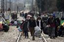 Migrants and refugees walk along train tracks as they wait to cross the Greek-Macedonian border near the Greek village of Idomeni, on 4 March, 2016