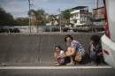 People take cover behind a concrete guardrail separating lanes on Avenida Brasil during a conflict between Brazilian Navy soldiers and alleged drug traffickers, near an entrance of Vila do Joao slum, part of the Complexo da Mare, in Rio de Janeiro, Brazil, Wednesday, Oct. 1, 2014. Pictured in the background are Navy armored vehicles and soldiers. (AP Photo/Felipe Dana)