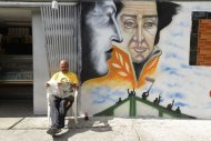 A man reads the newspaper next to graffiti depicting Venezuelan President Hugo Chavez (L) and South American independence hero Simon Bolivar, in Caracas, on January 2, 2013. Venezuela's main opposition movement demanded Wednesday that the government tell "the truth" about Chavez's health as one of his closest allies said his condition was "very worrying."